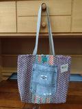 Lavender hand-woven tote bag with a light blue denim front pocket and silver shoulder straps