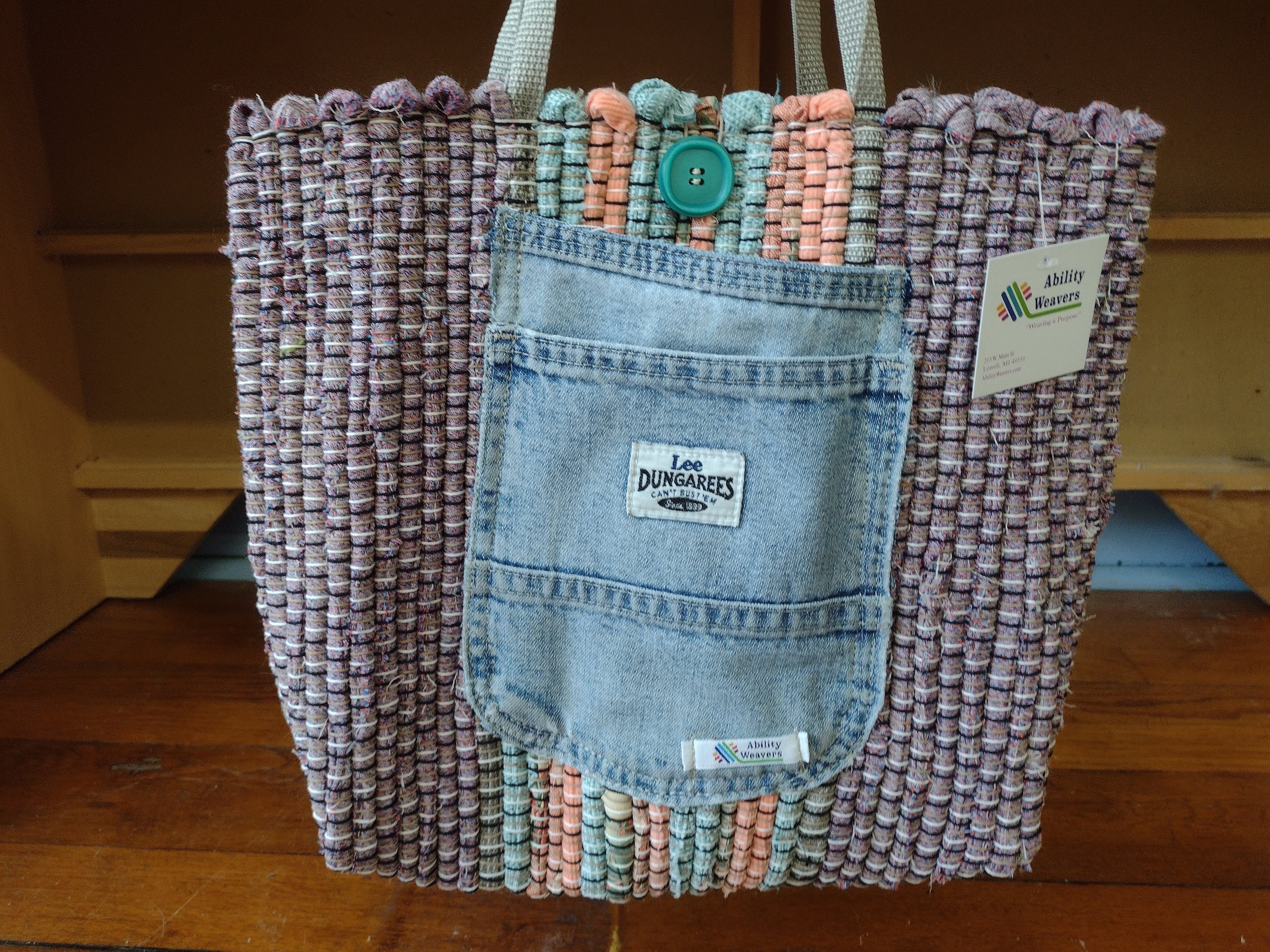 A handmade woven tote bag featuring a light blue denim front pocket with a 'Les Dungarees' label, set against a purple and white woven body with pastel pink accents and silver shoulder straps.