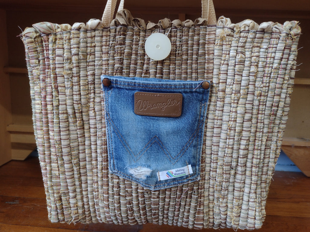 A woven tan & light brown tote bag with a blue denim back pocket featuring a brown leather patch that reads Wrangler.