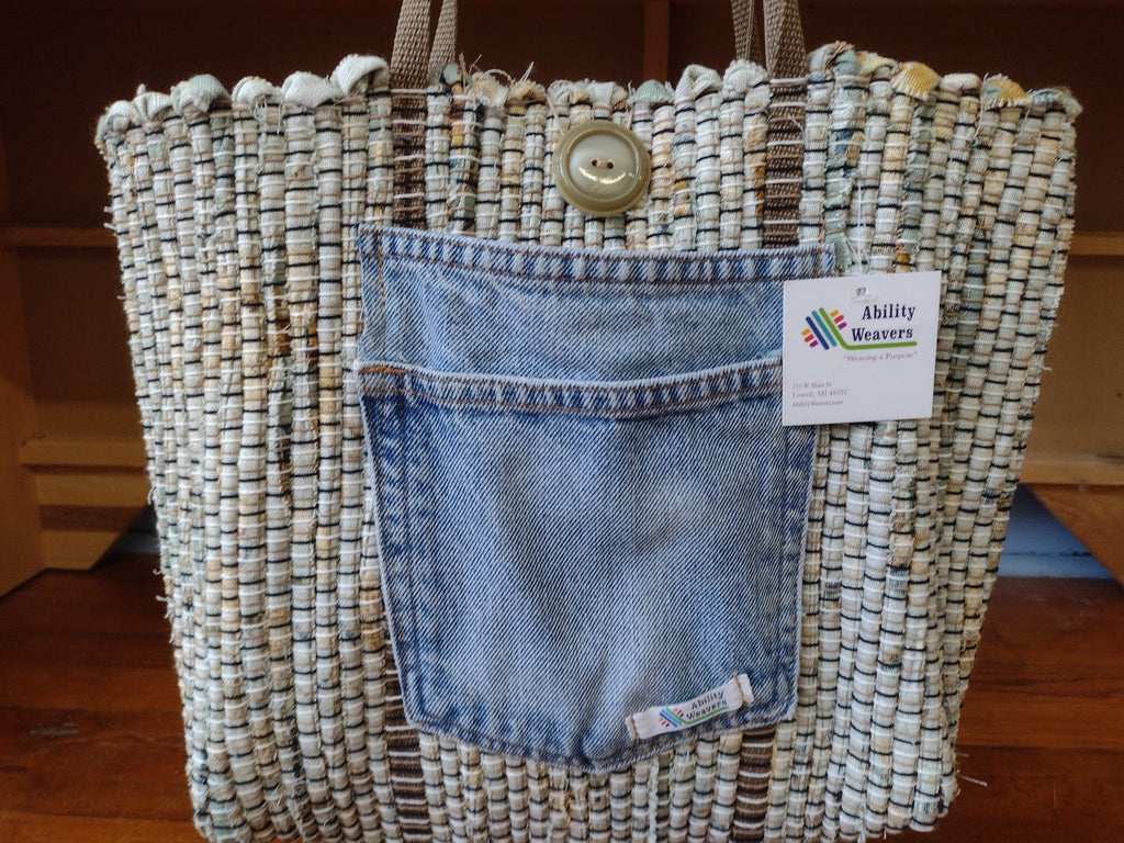 A handwoven sage color tote bag with  light brown strap and denim pocket.